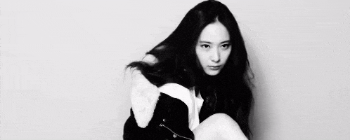 a black and white photo of a woman with long hair sitting on the floor .