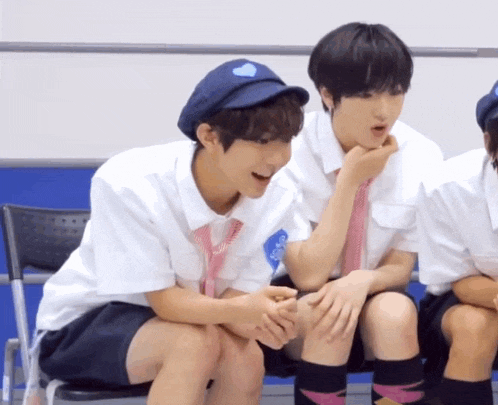 a boy wearing a blue hat with a heart on it sits next to another boy