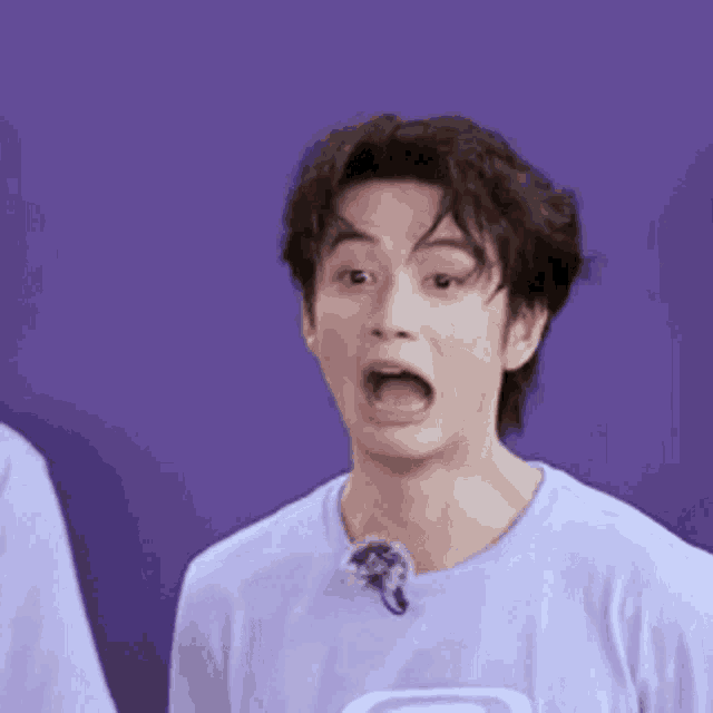 a man in a purple shirt is making a funny face while standing in front of a purple wall .