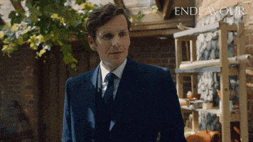 a man in a suit and tie is standing in front of a shelf with the word endeavour written on it