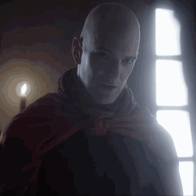 a bald man with a red cape around his neck looks at the camera