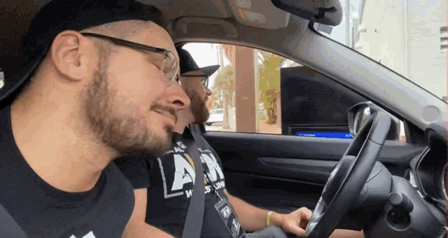 two men are sitting in a car with one wearing a shirt that says army