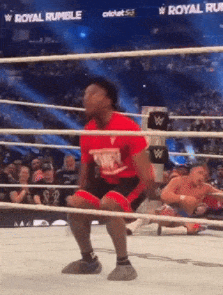 a man in a red shirt is squatting in a wrestling ring