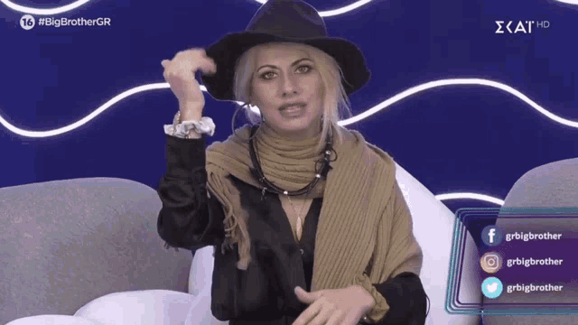 a woman wearing a hat and scarf is sitting on a couch in front of a big brother gr logo