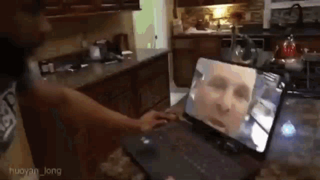 a person is using a laptop computer in a kitchen with a picture of a person on the screen .