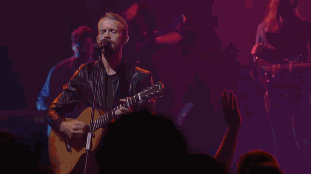 a man singing into a microphone while playing a guitar with a cross in the background