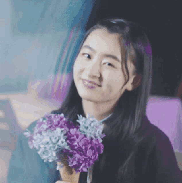 a young woman is holding a bouquet of purple flowers in her hand .