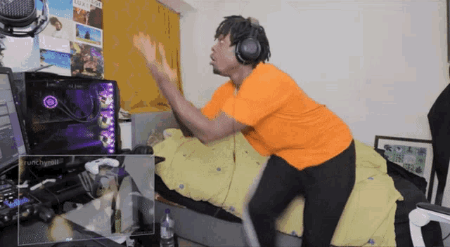 a man wearing headphones and an orange shirt is standing in front of a computer monitor with a purple circle on it