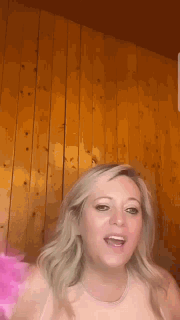 a woman is standing in front of a wooden wall and talking to the camera .