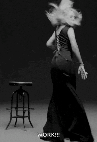 a woman in a long black dress is dancing in front of a stool with the word work written on it
