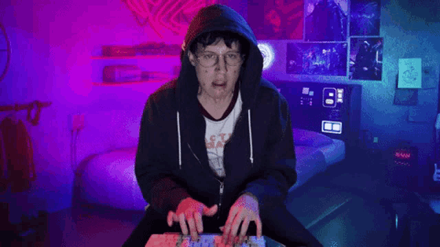 a man in a hoodie is typing on a keyboard in a bedroom