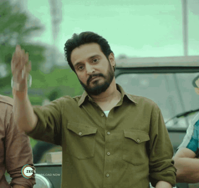 a man in a green shirt waves his hand in front of a sign that says zee