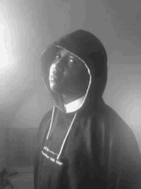 a black and white photo of a man wearing a hoodie and looking up .