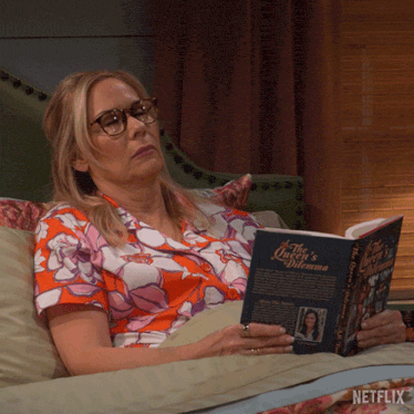 a woman is laying on a couch reading a book called the queen 's dilemma
