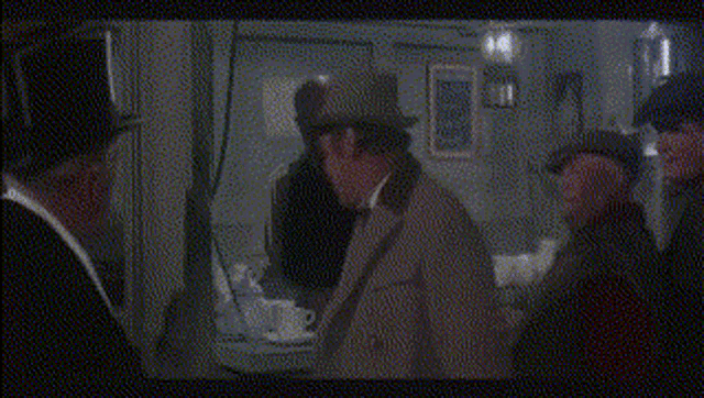 a man in a hat is talking to another man in a dark room .