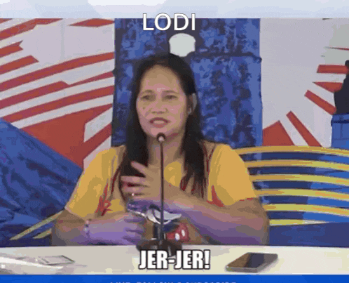 a woman is sitting at a table with a microphone and says lodi jer-jer!
