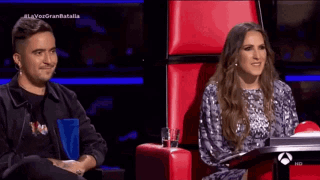 a man and a woman are sitting next to each other on a television show called la voz gran batalla .
