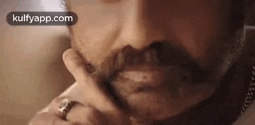 a close up of a man 's face with a ring on his finger and a beard .