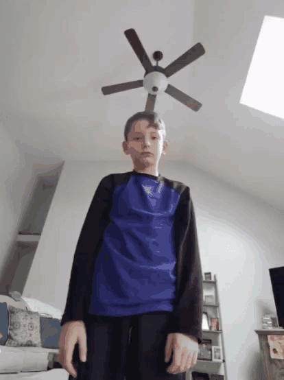 a boy standing in front of a ceiling fan