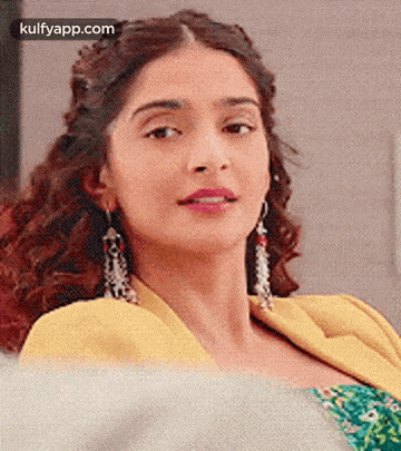 a close up of a woman wearing a yellow jacket and earrings looking at the camera .