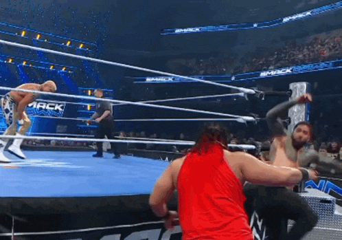 a man in a red tank top is standing in a wrestling ring with a referee