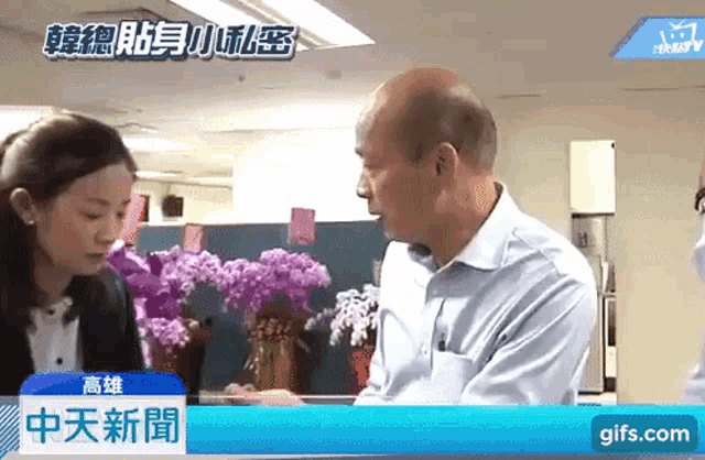 a man and a woman are talking in front of flowers and a gifs.com logo