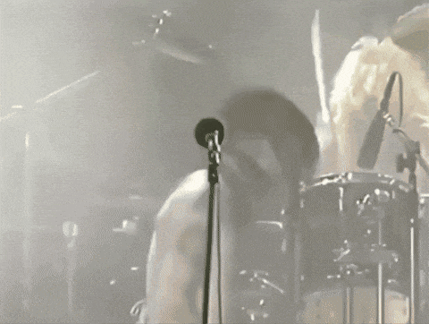 a man is singing into a microphone while another man plays drums
