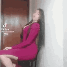 a woman in a red dress is sitting on a chair against a wall .