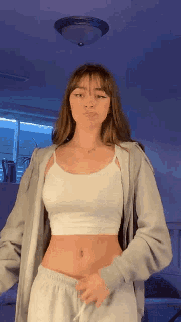 a woman is wearing a white crop top and a grey hoodie .