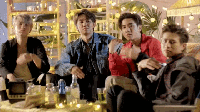a group of young men are sitting around a table with bottles