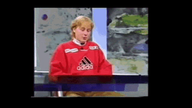 a man wearing a red adidas sweater is sitting at a table .