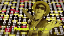 a man in a hat and sunglasses is standing in front of a screen that says welcome to ancapistan ..