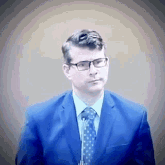a man in a blue suit and tie is looking at the camera .