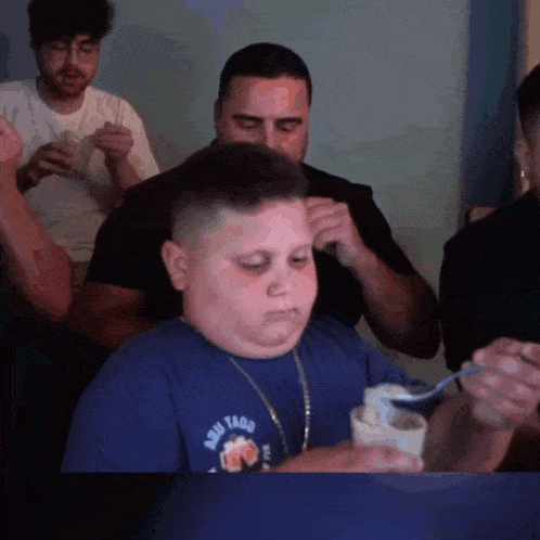 a boy wearing a shirt that says aqui tacos is eating something with a spoon