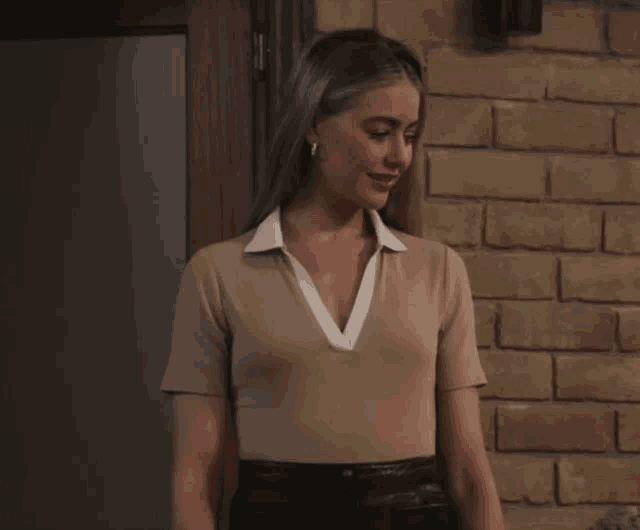 a woman standing in front of a brick wall wearing a tan top