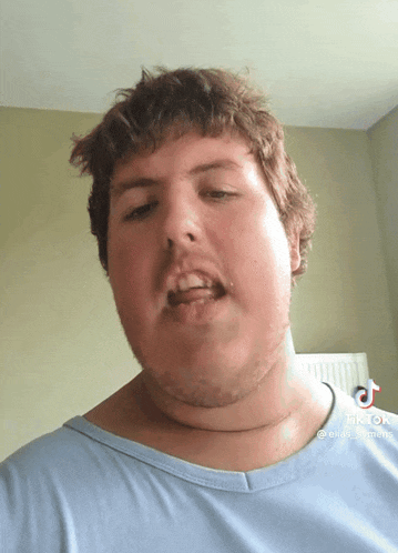 a man with a beard is wearing a blue shirt and has a tiktok sticker on his neck