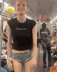 a woman is standing on a subway train wearing shorts and a black shirt .