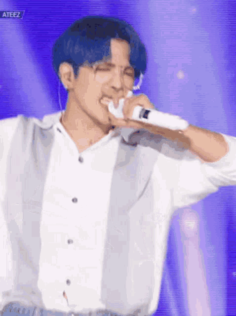 a man with blue hair is singing into a microphone while wearing glasses .