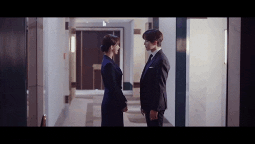 a man and a woman are standing next to each other in a hallway looking at each other