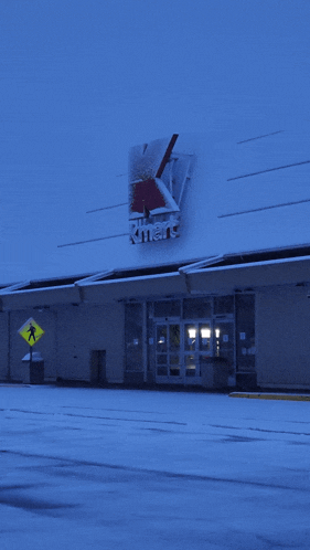 a kmart store is covered in snow and has a pedestrian crossing sign in front of it