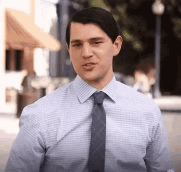 a man in a shirt and tie is making a funny face while standing on a street .