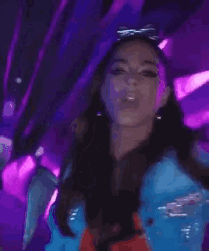 a woman in a blue jacket is dancing in a club with purple lights .