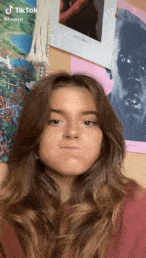 a girl is making a funny face in front of a wall with posters on it and a tiktok sticker