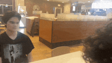 a young man wearing a black shirt with a picture of a hand on it stands in a restaurant