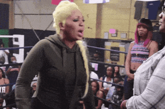 a woman in a green hoodie is standing in a boxing ring talking to another woman .
