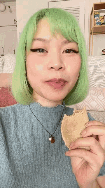 a woman with green hair holds a piece of food in her hand