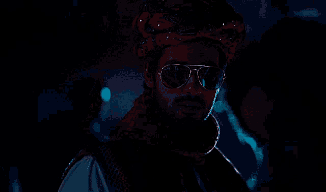 a man wearing sunglasses and a turban stands in a dark room