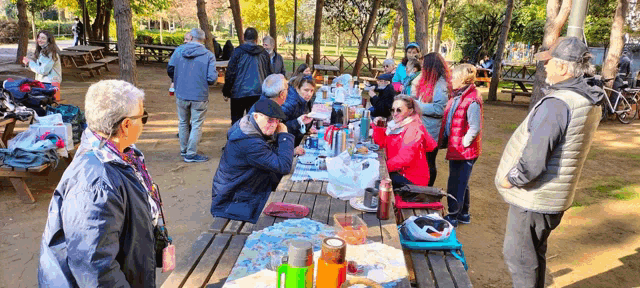 a group of people are gathered around a picnic table in the woods