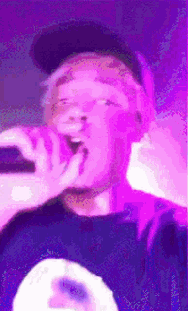a man is singing into a microphone while wearing a hat and a purple shirt .