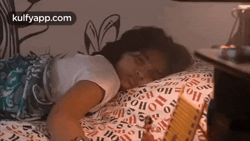 a young girl is sleeping on a bed with a book in her hand .